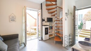 Ein modernes Wohnzimmer mit grauem Sofa, Fernseher, Bücherregal, Wendeltreppe und einer Tür zu einem Außenbereich.