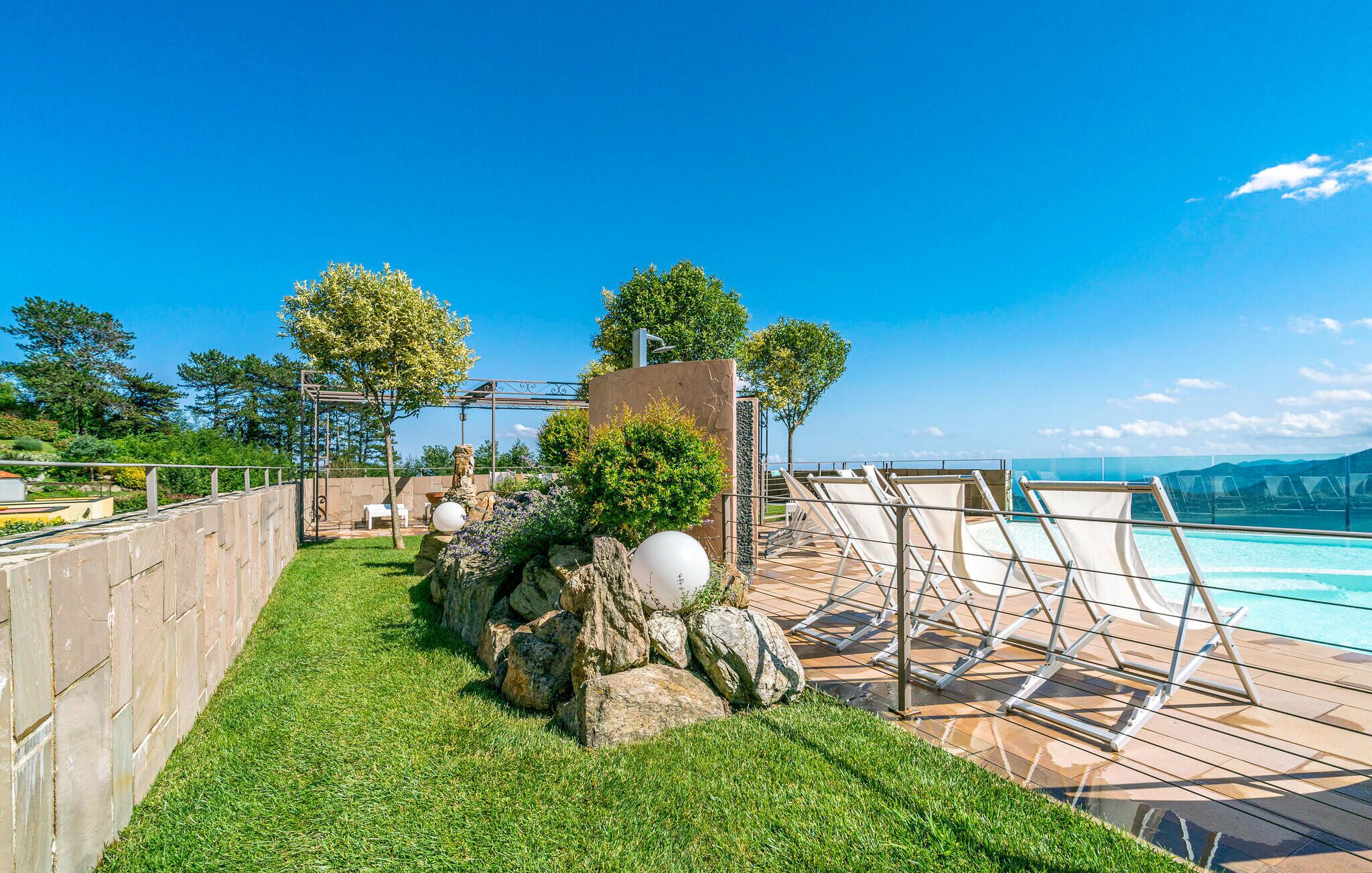 A rooftop pool area with a clear view of the ocean, surrounded by a well-maintained lawn and a pergola.