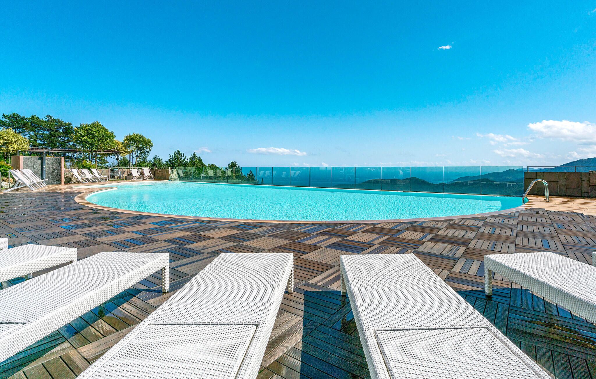 A pool area with a clear view of the ocean, surrounded by lounge chairs and a wooden deck.