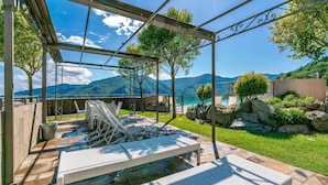 Eine Terrasse im Freien mit einer Pergola, Liegestühlen und Blick auf Berge und einen See.