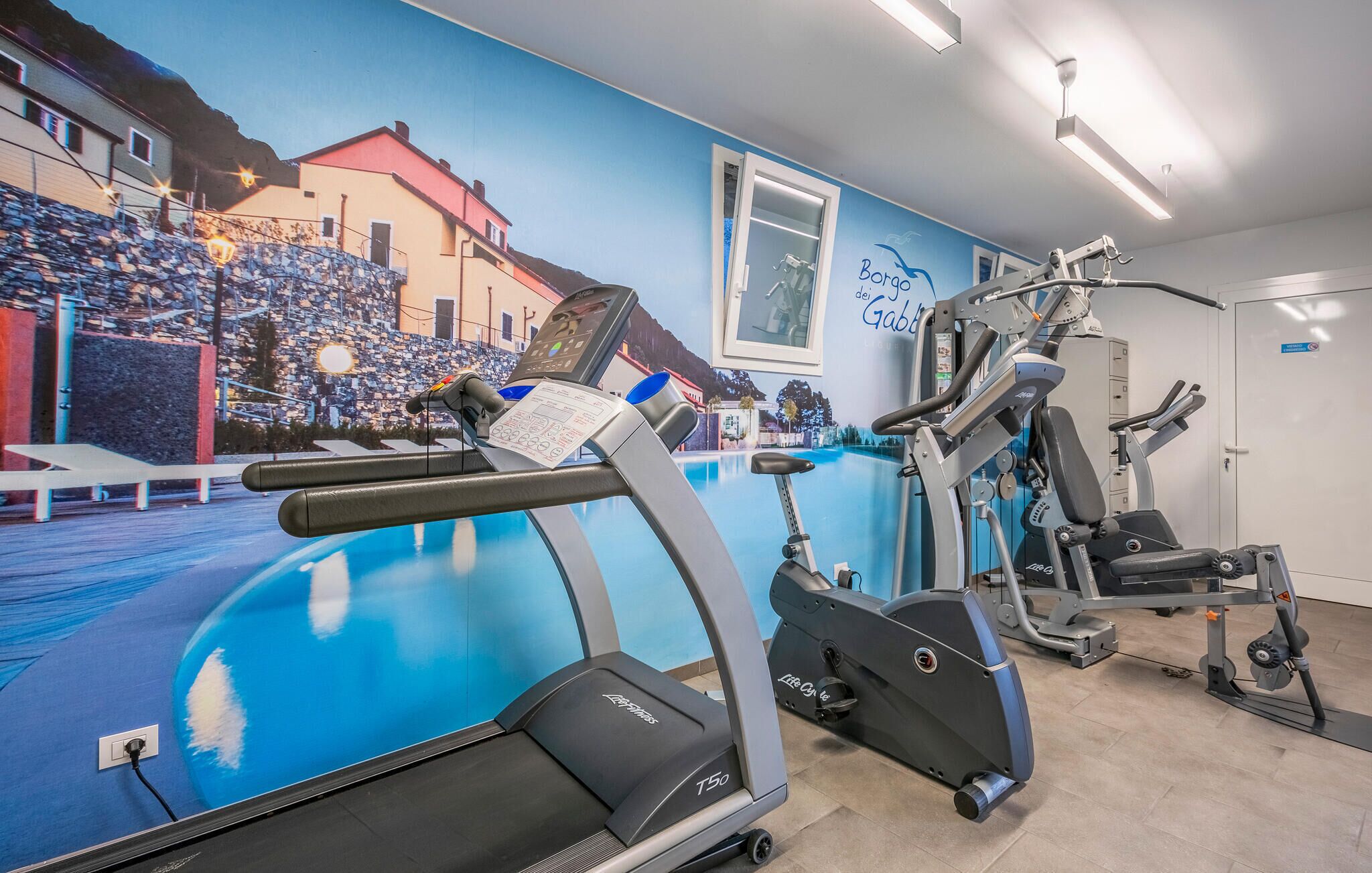 Een sportschool met loopbanden, een hometrainer en een krachttrainingapparaat.
