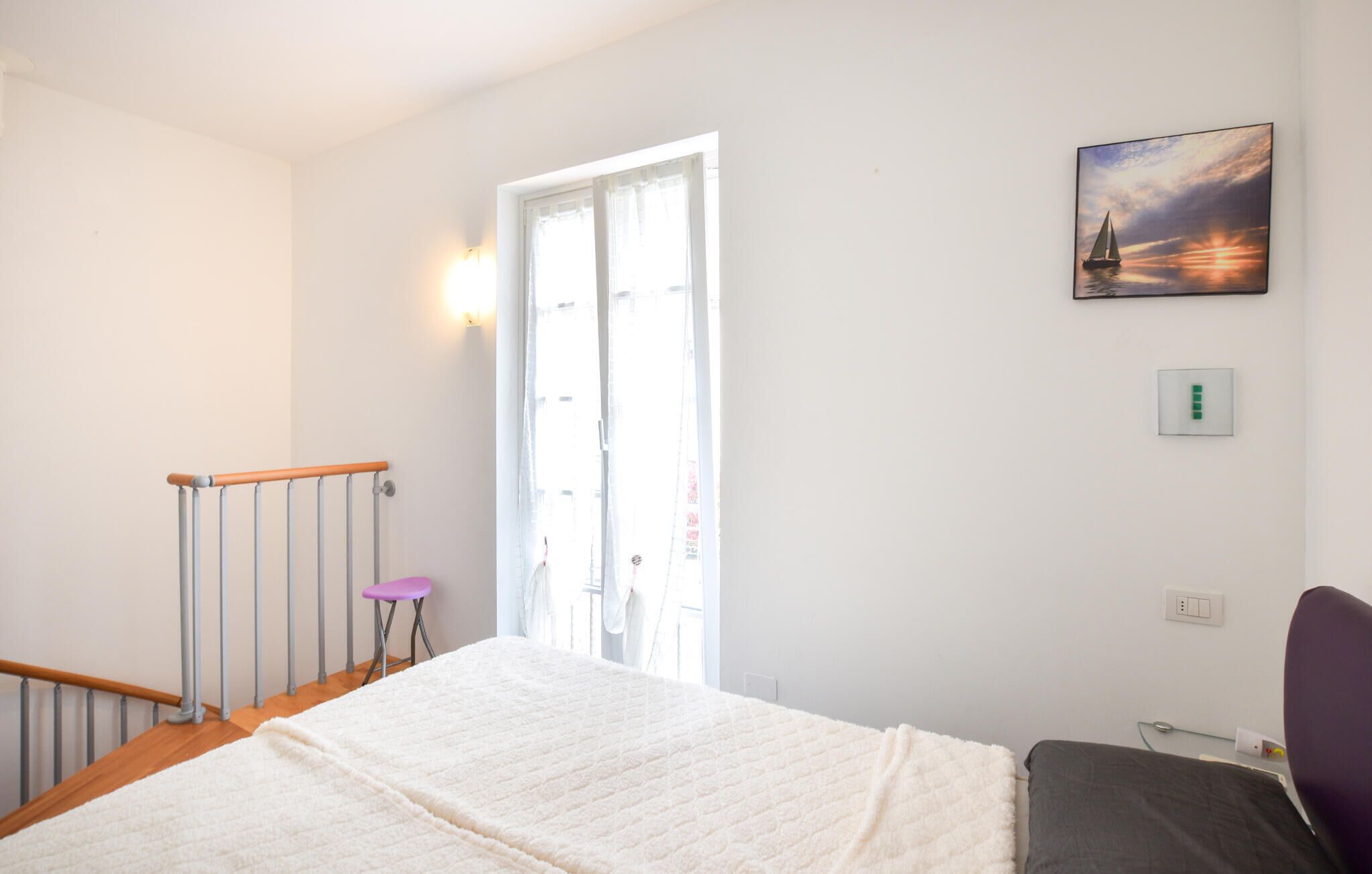 Ein Schlafzimmer mit Bett, Fenster, Gemälde und Stuhl.