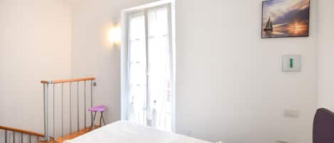 Ein Schlafzimmer mit Bett, Fenster, Gemälde und Stuhl.