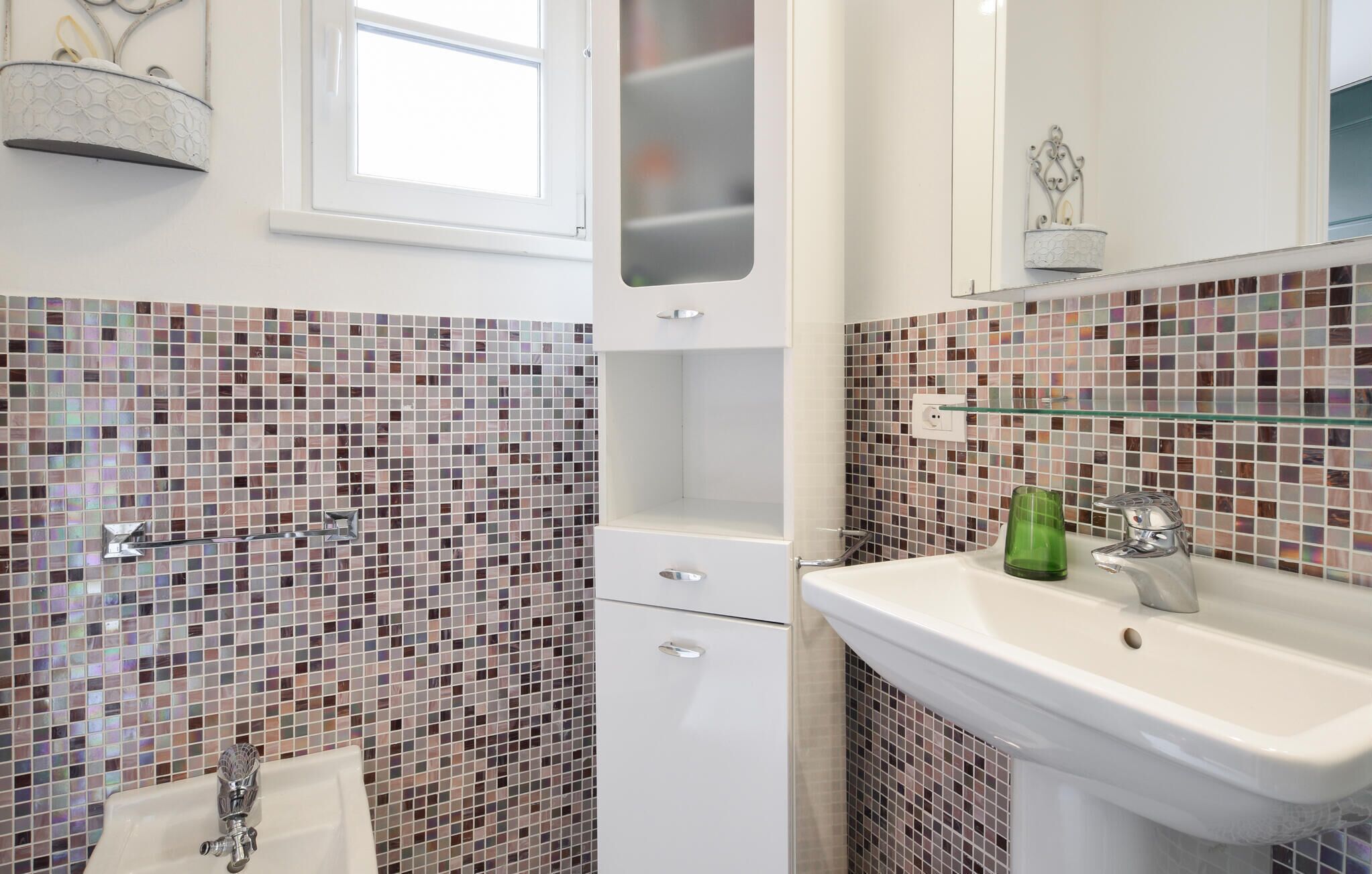 A bathroom with a tiled mosaic backsplash, a white sink with a green glass, and a mirror above the sink.