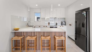 Eine moderne Küche mit weißen Schr änken, einem schwarzen Kühlschrank und drei Holzbarhocker.