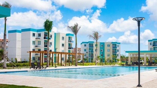 A swimming pool with lounge chairs, a pergola, and multi-story buildings with balconies. - Vacation in punta cana (Punta Cana)