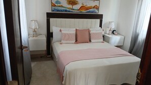 A bedroom with a bed, two bedside tables, a nightstand, a painting on the wall, and a door. - Vacation in punta cana (Punta Cana)