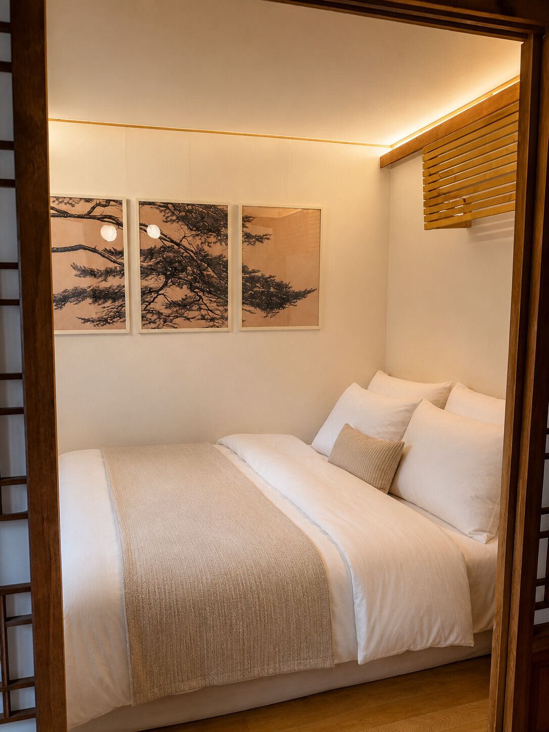 A bedroom with a bed, pillows, a blanket, and three framed artworks on the wall.