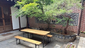 Un patio con una mesa y bancos de madera, un muro de ladrillo con diseños decorativos y una pequeña zona ajardinada con plantas.