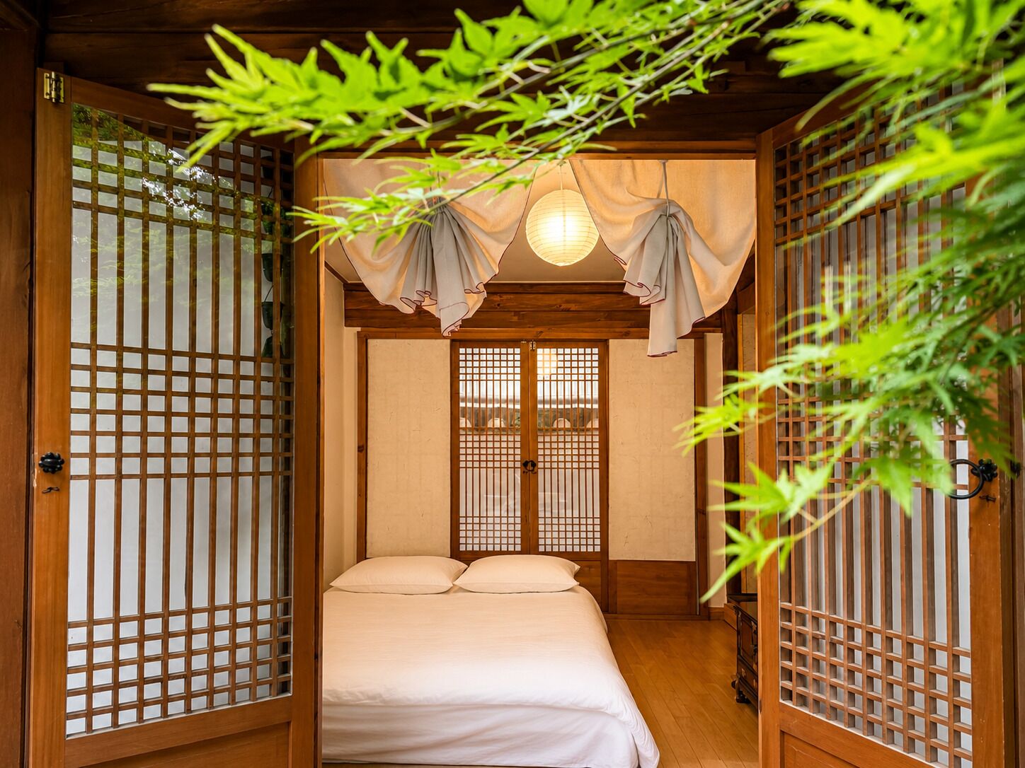 Une pièce de style japonais traditionnel, avec un sol recouvert de tatamis, un lit bas, des portes coulissantes à motifs géométriques et un luminaire suspendu.