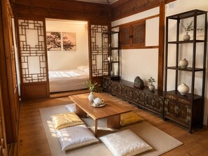 Une pièce de style japonais traditionnel, avec un sol recouvert de tatamis, une basse table en bois, des coussins, une porte coulissante et une étagère ornée d’objets décoratifs.