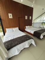 A hotel room with two beds, wooden paneling on the walls, and a balcony with a railing.