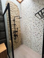 A bathroom with a stone wall, a shower with a black faucet, and a terrazzo floor.