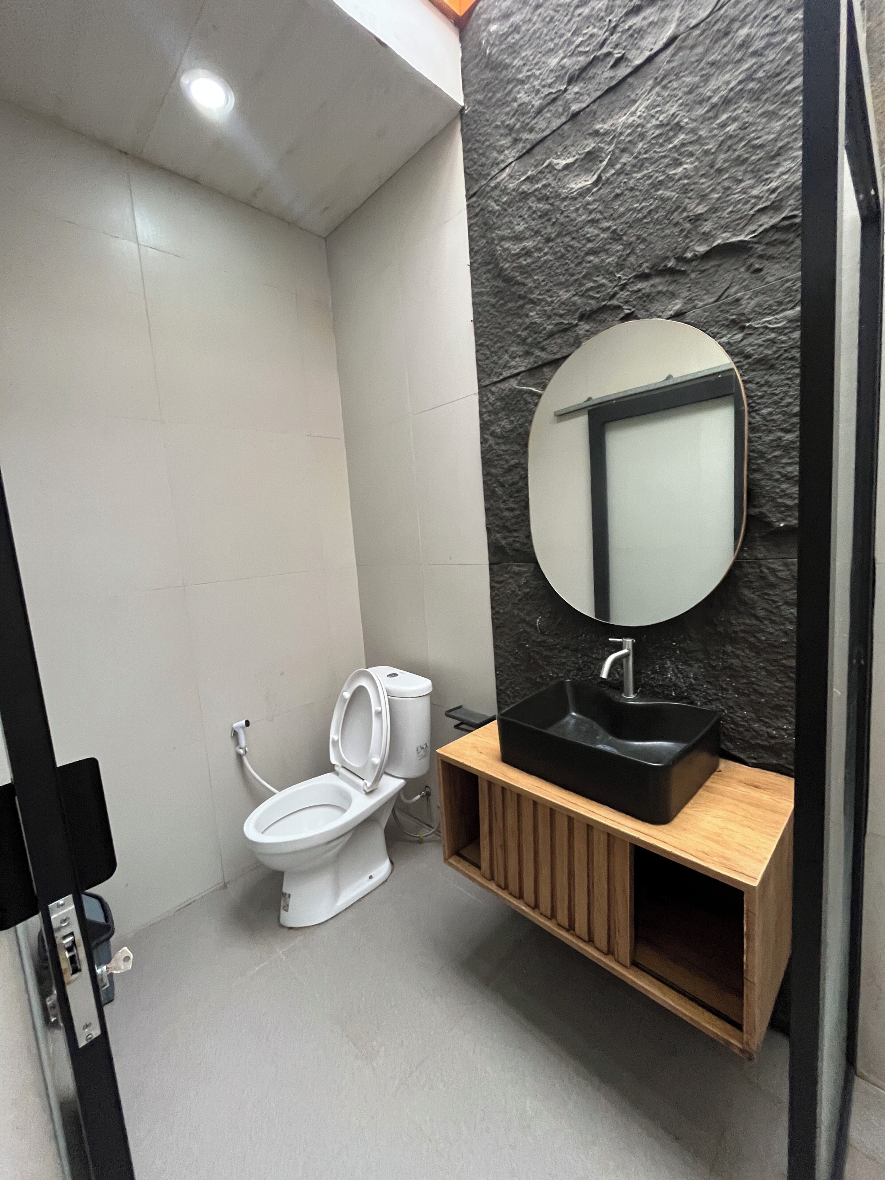 A modern bathroom with a white toilet, a black sink, and a mirror.