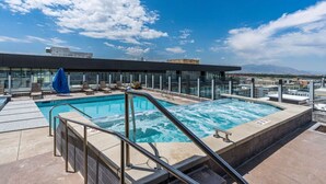 Ein Pool auf dem Dach mit klarem, blauem Wasser, umgeben von Liegestühlen und einer Glasschutzwand.