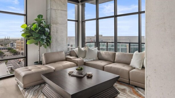 Ein modernes Wohnzimmer mit einer Eckcouch, einem Couchtisch und einem großen Fenster mit Blick auf die Stadt.