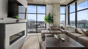 Ein modernes Wohnzimmer mit großem Fenster, einer Couch, einem Couchtisch und einem an der Wand befestigten Fernseher.