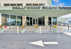 Der Eingang zum Hollywood Beach Tower mit freiem Blick auf den Schriftzug des Gebäudes, einer Treppe, die zum Eingang führt, und Richtungspfeilen auf dem Boden.