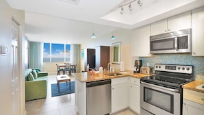 A modern kitchen with stainless steel appliances, a dining area with a green sofa, and a view of the sky through large windows. - Cozy Studio condo with AC in amazing Hollywood (Hollywood)