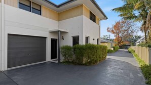 A modern two-story residential building with a garage, a covered walkway, and a well-maintained garden. - Coastal Cove by Experience Jervis Bay (Huskisson)