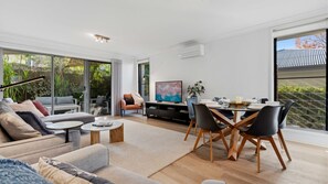 Ein modernes Wohnzimmer mit einer Couch, Couchtisch, Fernseher und einem Essbereich mit Stühlen und Tisch.