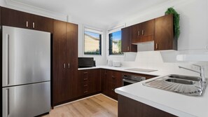 Eine moderne Küche mit dunklen Holzausführungen, einem Edelstahlkühlschrank, einem eingebauten Backofen, einer Spüle und einem Fenster mit Blick ins Freie.