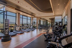 Ein modernes Fitnessstudio mit Laufbändern, Crosstrainern und Kraftgeräten. Große Fenster bieten Ausblicke ins Freie.