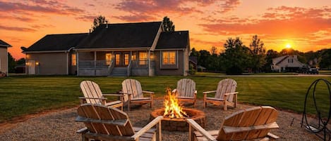 Una casa con fogata y sillas Adirondack en el jardín.