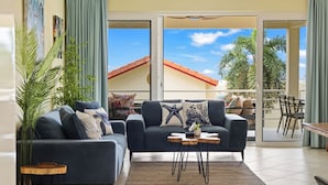 A living room with two sofas, a coffee table, and a view of a building with a red roof through large glass doors. - Casa Piscadera · Ocean View · Pool · Beaches (Piscadera)