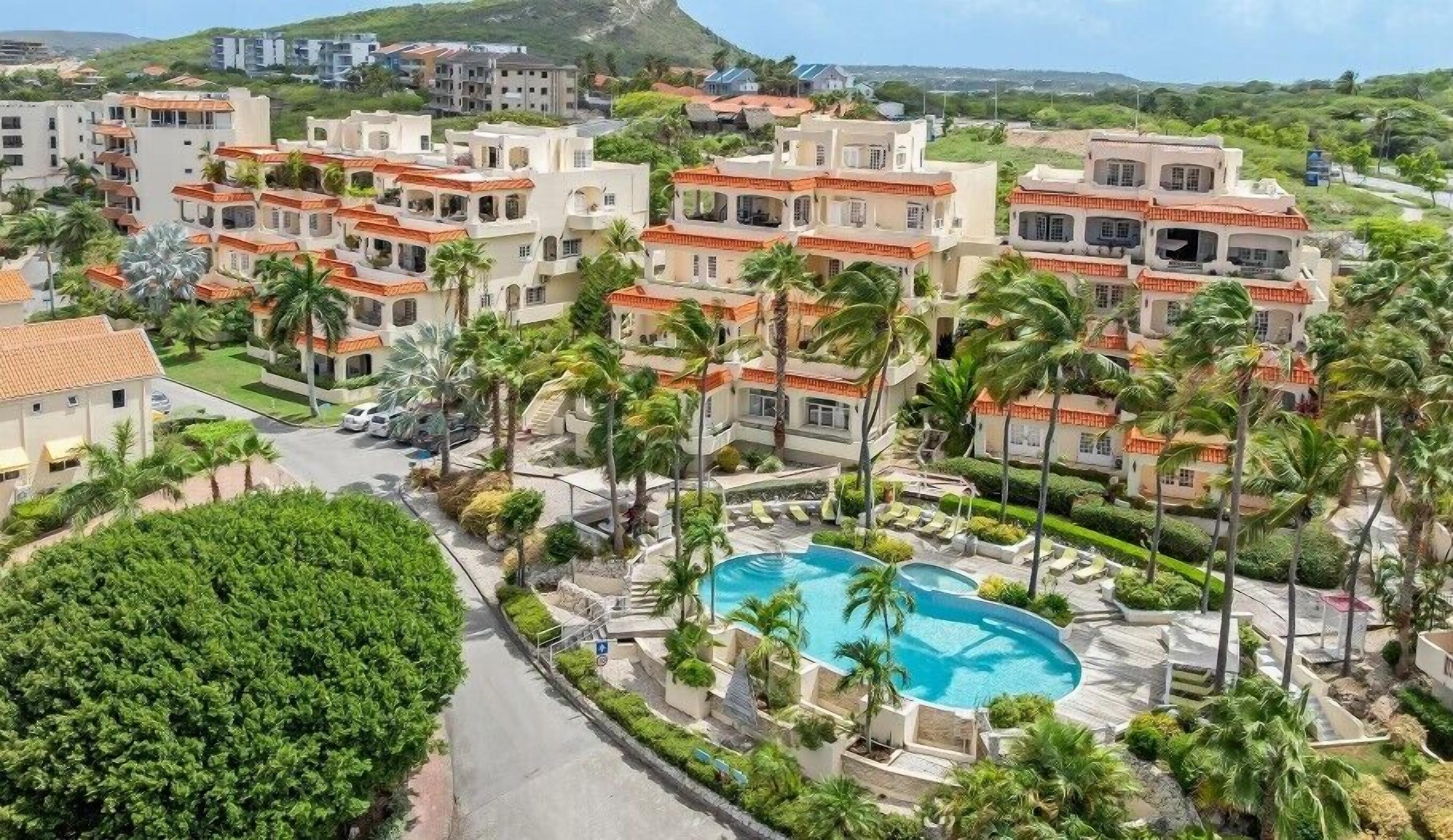 Et resort med flere etagers bygninger, en swimmingpool og palmer.