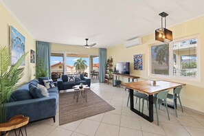 Ein Wohnzimmer mit einer Couch, Couchtisch, Fernseher, Esstisch, Stühlen und einem Balkon mit Aussicht.