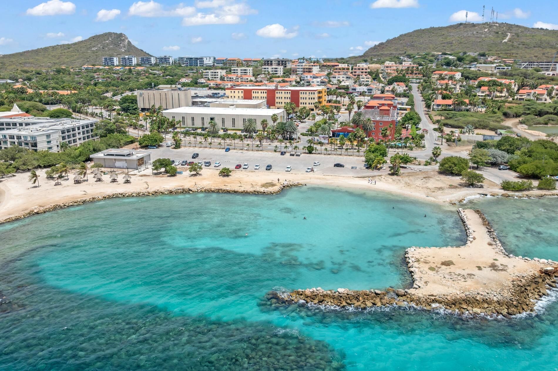 A coastal town with a beach, clear turquoise waters, and a mix of residential and commercial buildings.