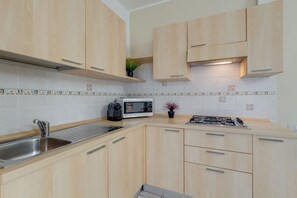 A modern kitchen with light wood cabinets, a stainless steel sink, a microwave, and a gas stove. - Porto Letizia Rossini 3, Porlezza, Italy (Porlezza)