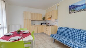 Une cuisine de taille réduite avec des meubles en bois, une table à manger dressée avec des assiettes et des couverts, un canapé bleu et un tableau représentant un paysage accroché au mur.