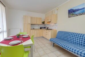 A compact kitchen with wooden cabinets, a dining table set with plates and cutlery, a blue sofa, and a painting of a landscape on the wall. - Porto Letizia Rossini 3, Porlezza, Italy (Porlezza)