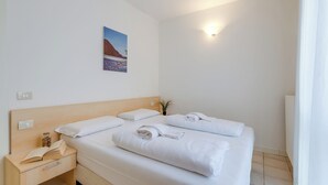 Une chambre d’hôtel avec un grand lit, une table de chevet avec un livre et une lampe, et un tableau accroché au mur.