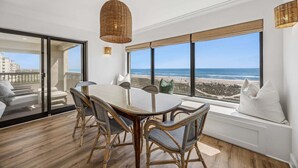 A dining area with a table and chairs, large windows with a view of the beach, and a wicker pendant light. - Luxury Oceanfront 2 bed 2 bath Condo - Stunning (Fernandina Beach)