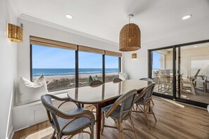 Ein Essbereich mit einem Glastisch, Korbstühlen und Blick auf den Strand.