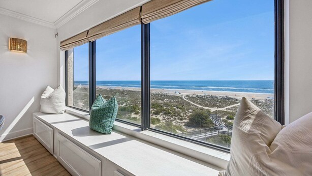 A room with a large window overlooking a beach, a built-in bench, and a small wall-mounted light fixture. - Luxury Oceanfront 2 bed 2 bath Condo - Stunning (Fernandina Beach)