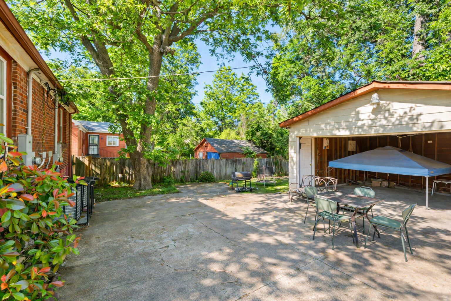 A backyard with a covered patio, a barbecue grill, and a fenced area.