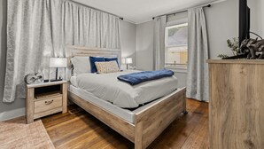 Une chambre à coucher avec un lit en bois, des tables de chevet, un ventilateur de plafond et une fenêtre avec des rideaux.