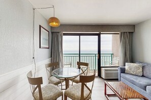A room with a balcony, a round table with chairs, a sofa, and a hanging light fixture. - Oceanfront studio with private balcony, pool & direct beach access (Myrtle Beach)