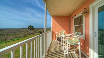 A balcony with two striped chairs, a white railing, and a view of the landscape.