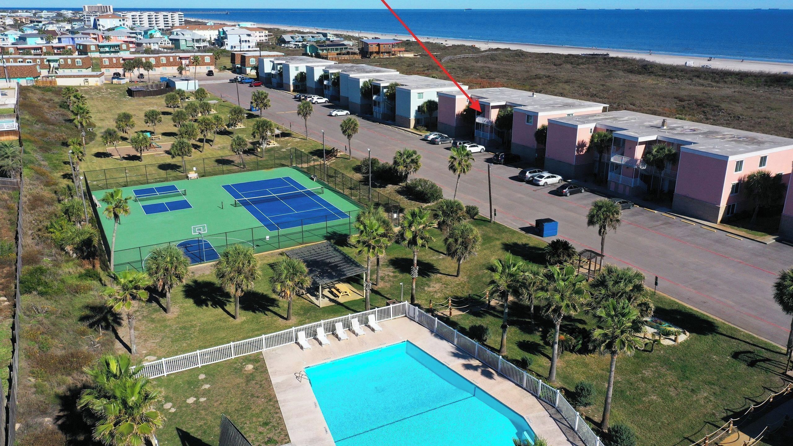 A residential area with a tennis court, pool, and beachfront view.