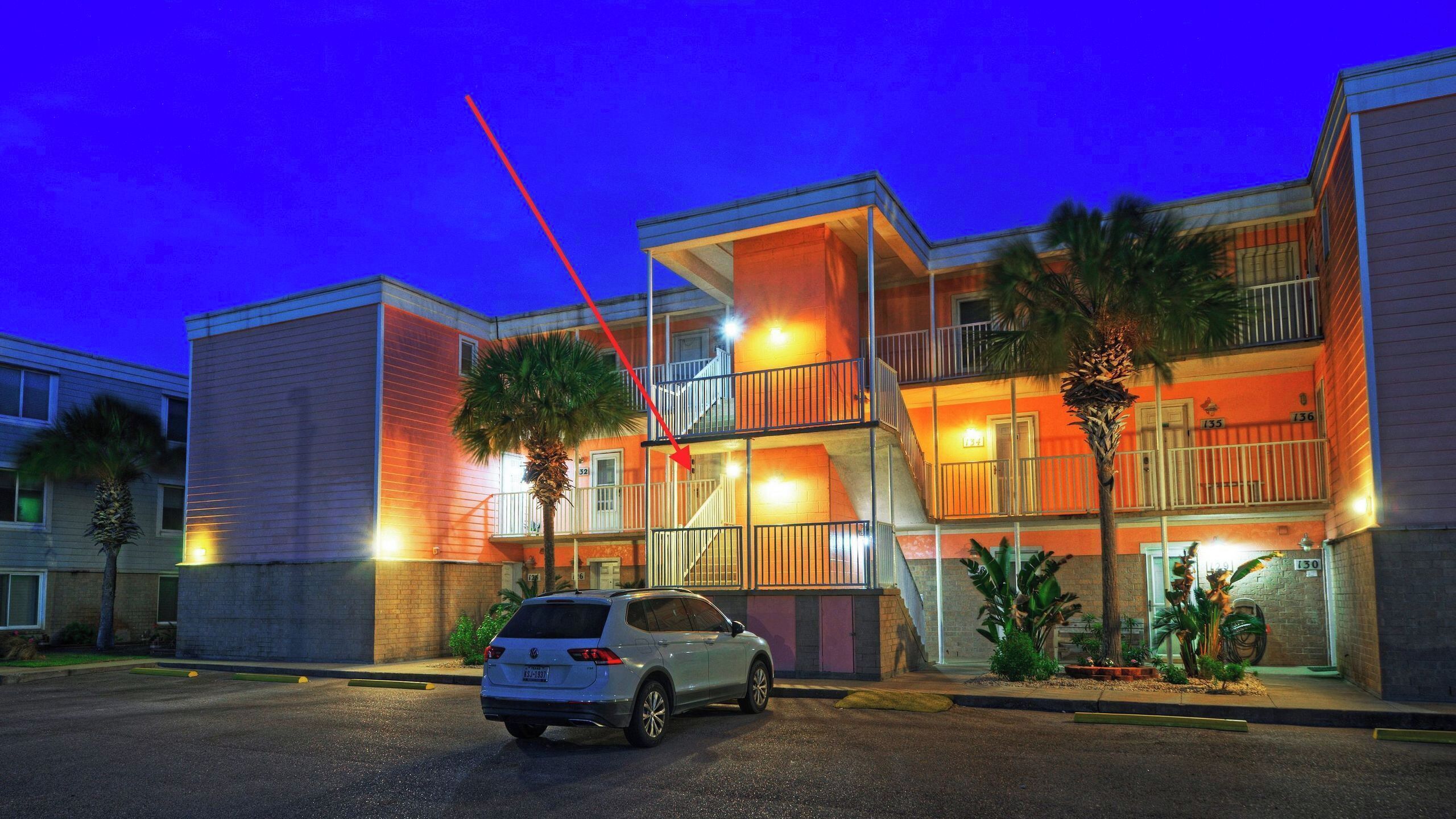 A multi-story hotel with balconies, a parking lot, and palm trees.