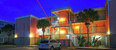 A multi-story hotel with balconies, a parking lot, and palm trees.