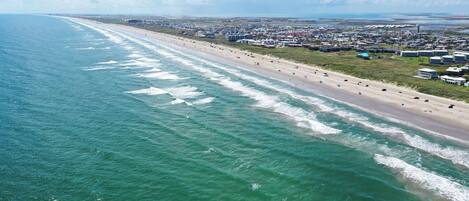 An aerial view of a coastal area with a beach, buildings, and a clear sky.