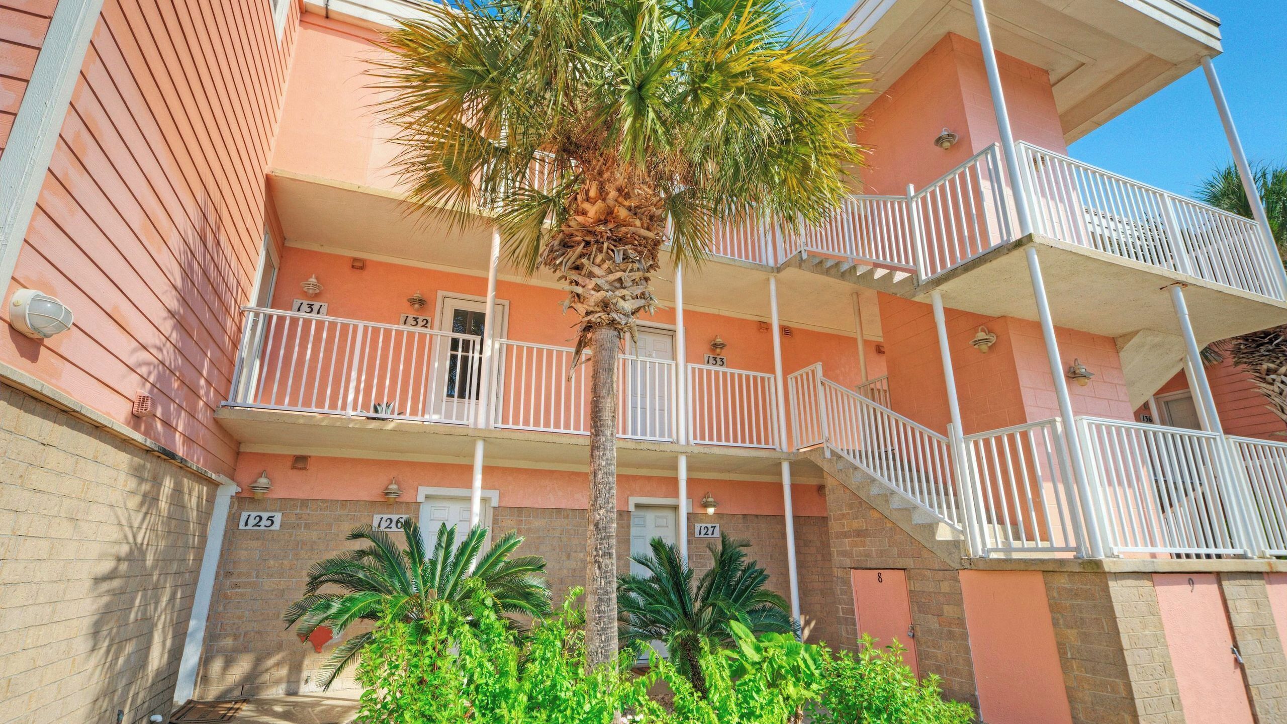 A multi-story building with balconies, numbered doors, and a palm tree.