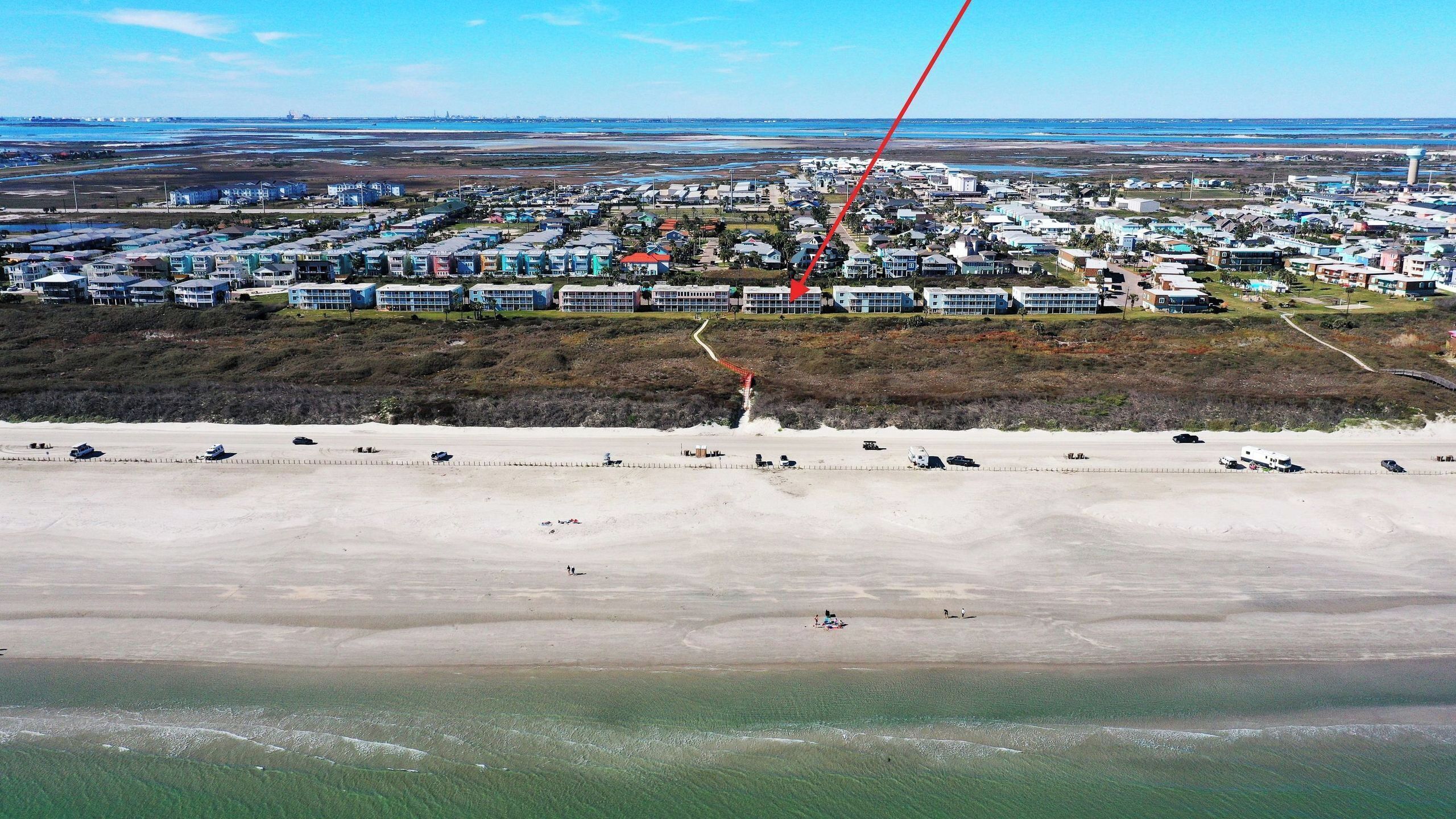 Vue aérienne d’une ville côtière avec une plage, des immeubles résidentiels et un ciel dégagé.