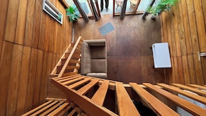 A wooden interior with a staircase, a cushioned seating area, and a small potted plant. - Cabin Dieng Db (Dieng Kulon)